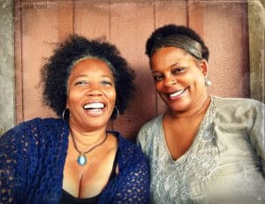 A photo of Lisa Sanders and Brown Sugar smiling at the camera with a wood backdrop.